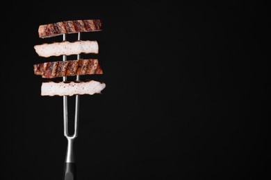 Carving fork with cut grilled pork steak pieces against black background. Space for text