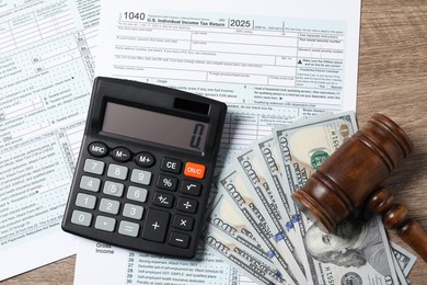 Tax return forms, dollar banknotes, calculator and gavel on wooden table, top view