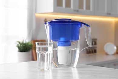 Water filter jug and glass on white marble table in kitchen, closeup