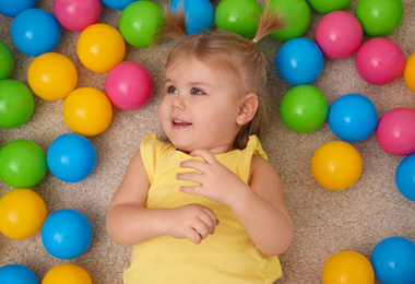 Photo of Cute little child playing with balls on floor, top view