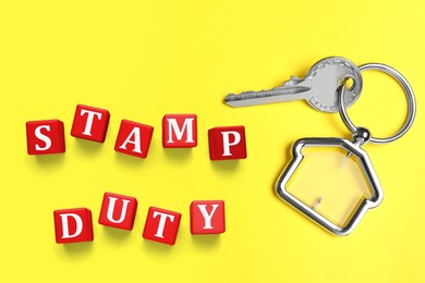 Key with trinket in shape of house and red cubes with text Stamp Duty on yellow background, top view