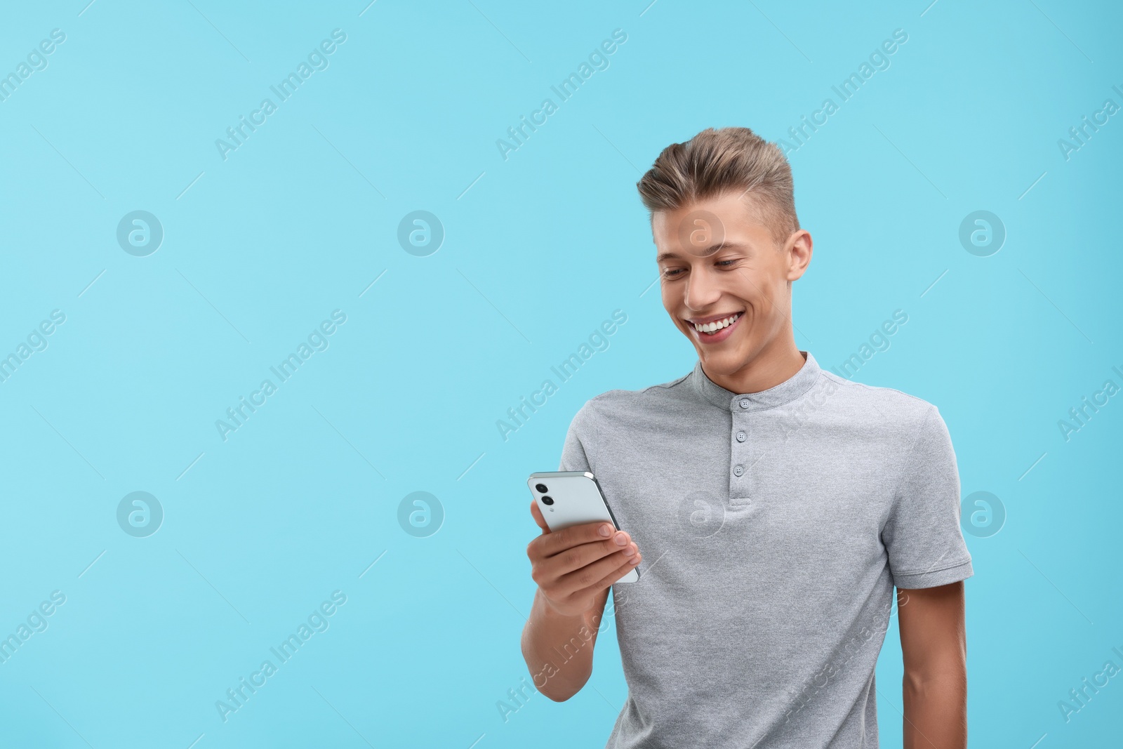 Photo of Happy young man sending message via smartphone on light blue background. Space for text