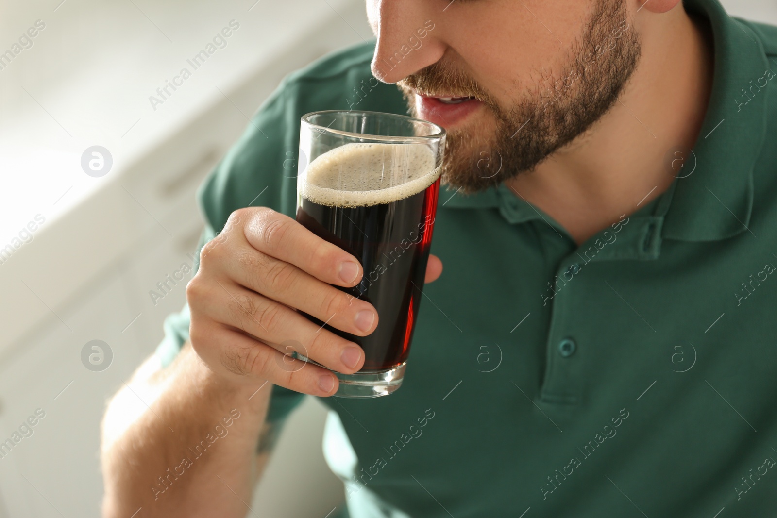 Photo of Young man with cold kvass indoors, closeup. Traditional Russian summer drink