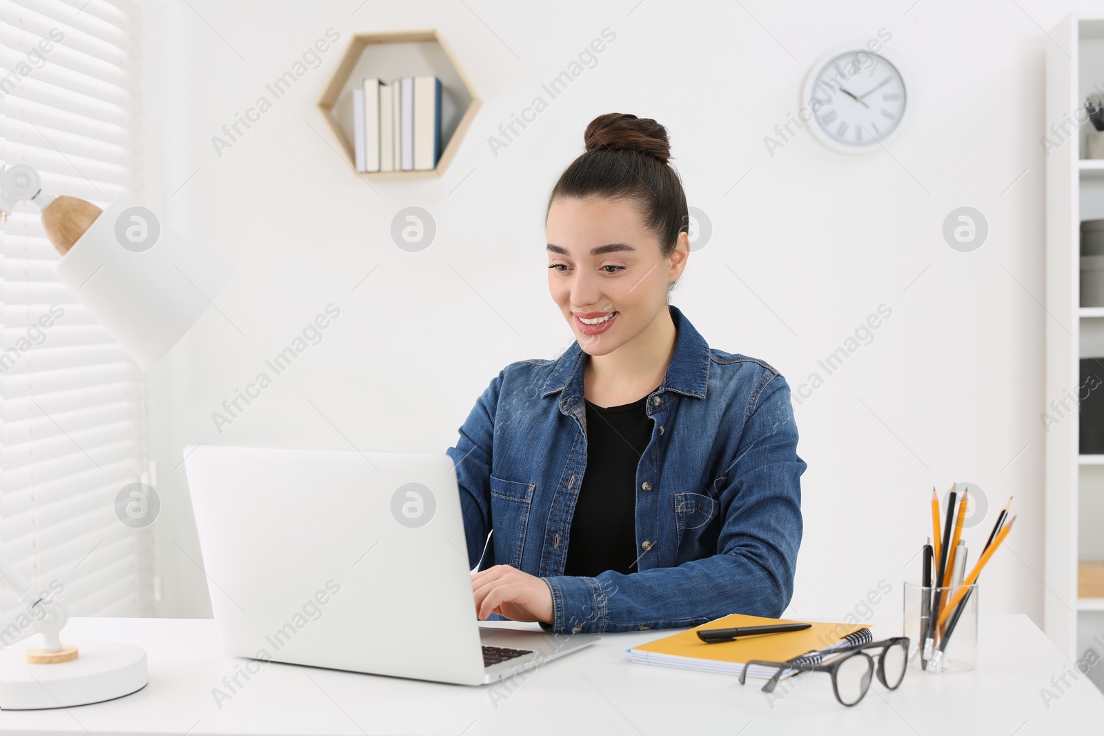 Photo of Home workplace. Happy woman typing on laptop at white desk in room