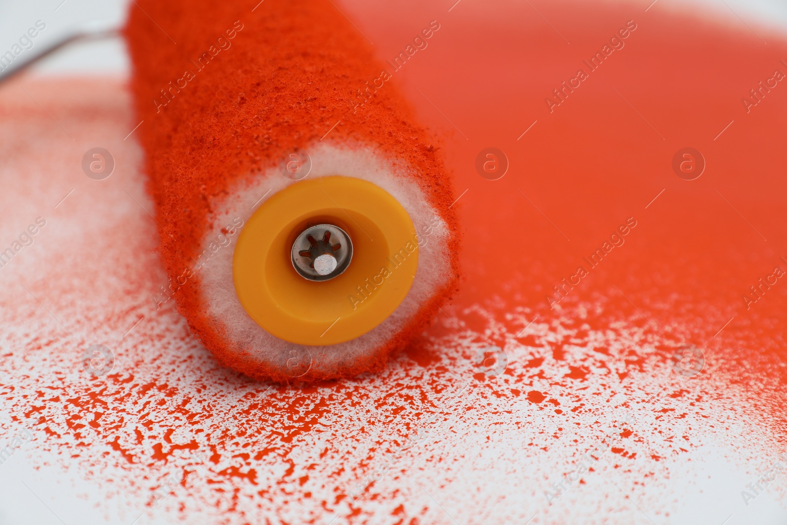 Photo of Roller brush and strokes of orange paint on white background, closeup