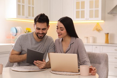 Photo of Happy couple in pajamas using gadgets at kitchen table