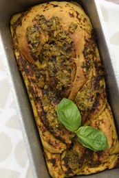 Photo of Freshly baked pesto bread with basil in loaf pan on table, top view