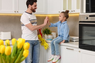 Photo of Spring cleaning. Father and daughter giving high five in kitchen