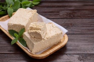 Photo of Pieces of tasty halva and mint on wooden table, closeup