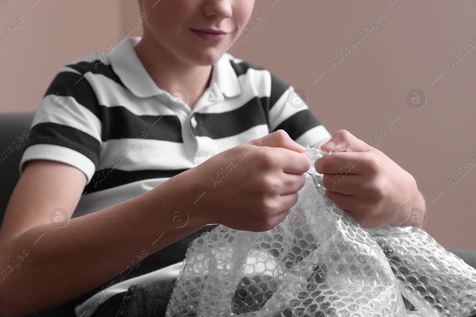 Photo of Boy popping bubble wrap indoors, closeup. Stress relief