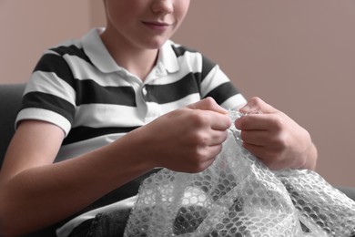 Boy popping bubble wrap indoors, closeup. Stress relief