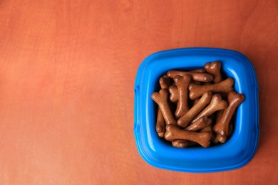 Photo of Blue bowl with bone shaped dog cookies on wooden table, top view. Space for text