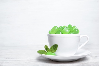 Photo of Cup with tasty mint candies and leaves on table