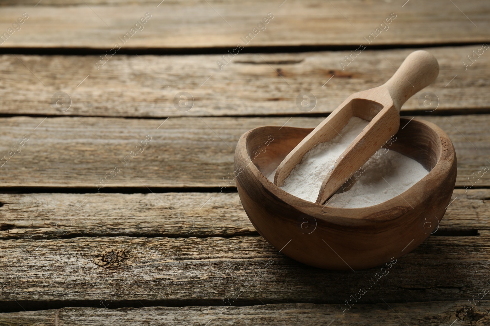 Photo of Baking powder in bowl and scoop on wooden table, space for text