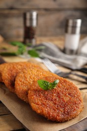 Photo of Delicious fried breaded cutlets with basil on wooden table