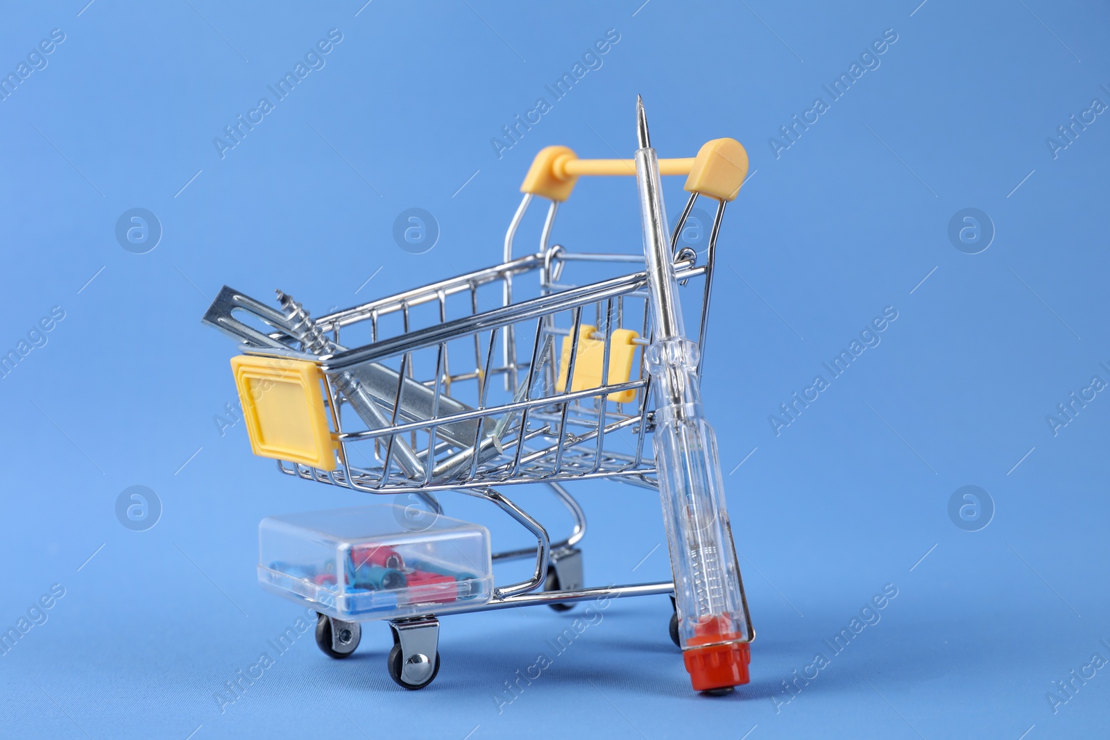 Photo of Small shopping cart with set of construction tools on light blue background