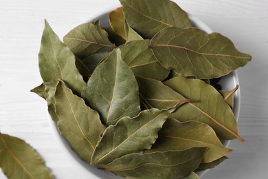 Photo of Dry bay leaves in bowl on white wooden table, closeup