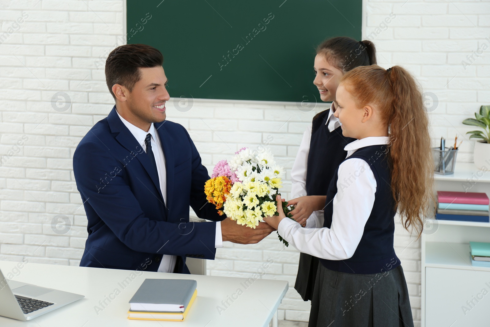 Photo of Schoolgirls congratulating their pedagogue with bouquet in classroom. Teacher's day