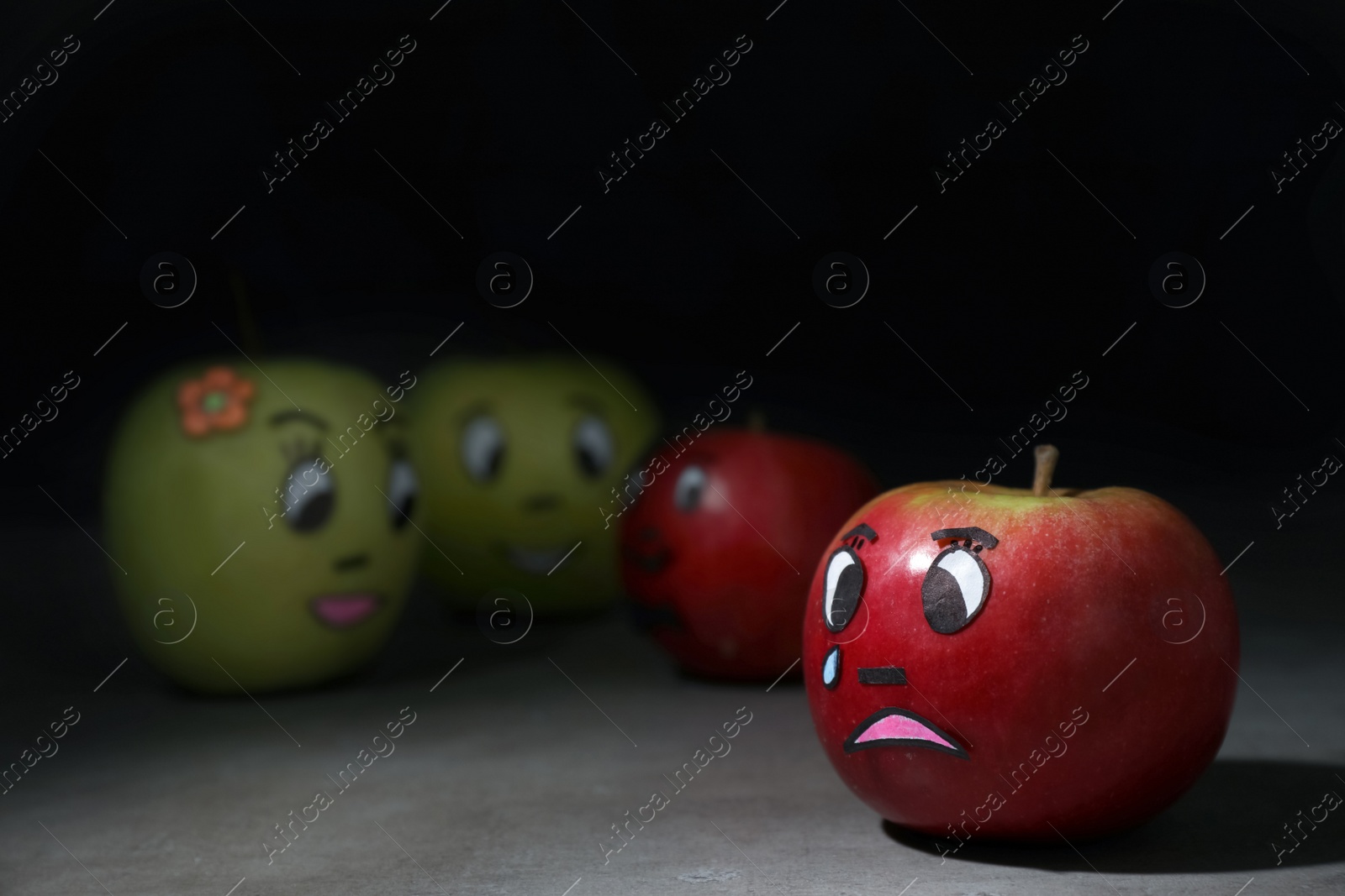 Photo of Apple with crying face on grey table. Concept of jealousy