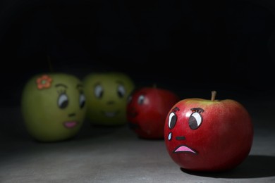 Photo of Apple with crying face on grey table. Concept of jealousy