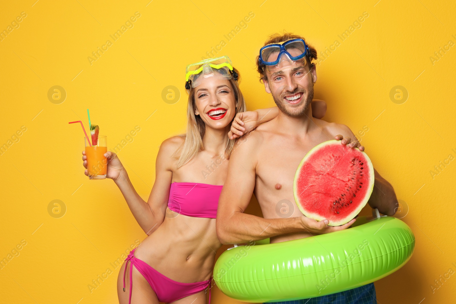 Photo of Happy young couple in beachwear with inflatable ring and cocktail on color background