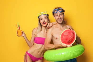 Photo of Happy young couple in beachwear with inflatable ring and cocktail on color background