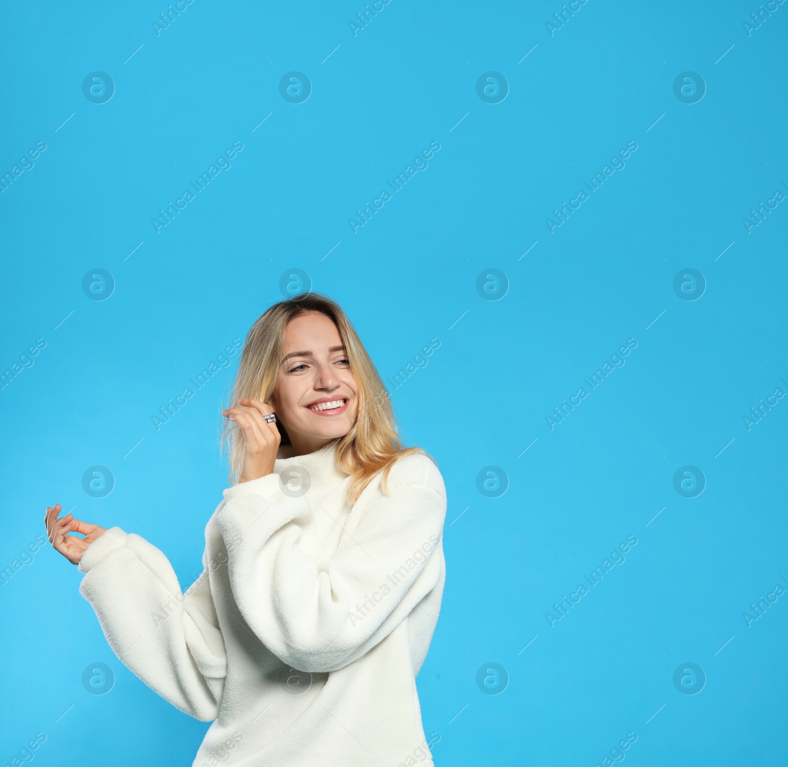 Photo of Beautiful young woman wearing knitted sweater on light blue background. Space for text