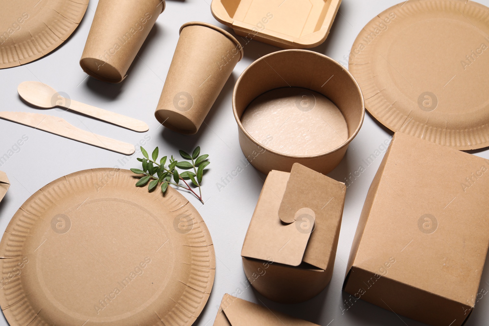 Photo of Eco friendly food packaging. Paper containers, tableware and green twigs on light grey background