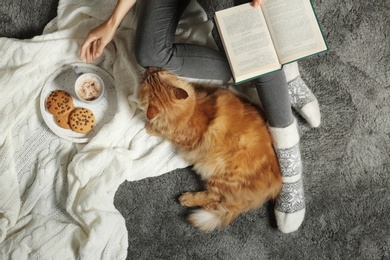 Woman with cute red cat and book on grey carpet, top view