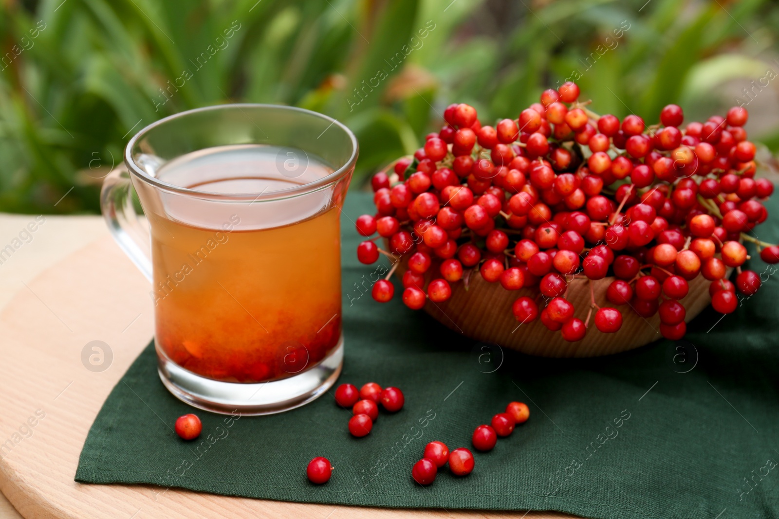 Photo of Cup of tea and fresh ripe viburnum berries on table outdoors