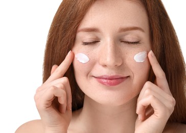 Beautiful woman with freckles applying cream onto her face against white background