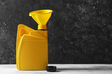 Photo of Yellow canister with motor oil and plastic funnel on white table. Space for text