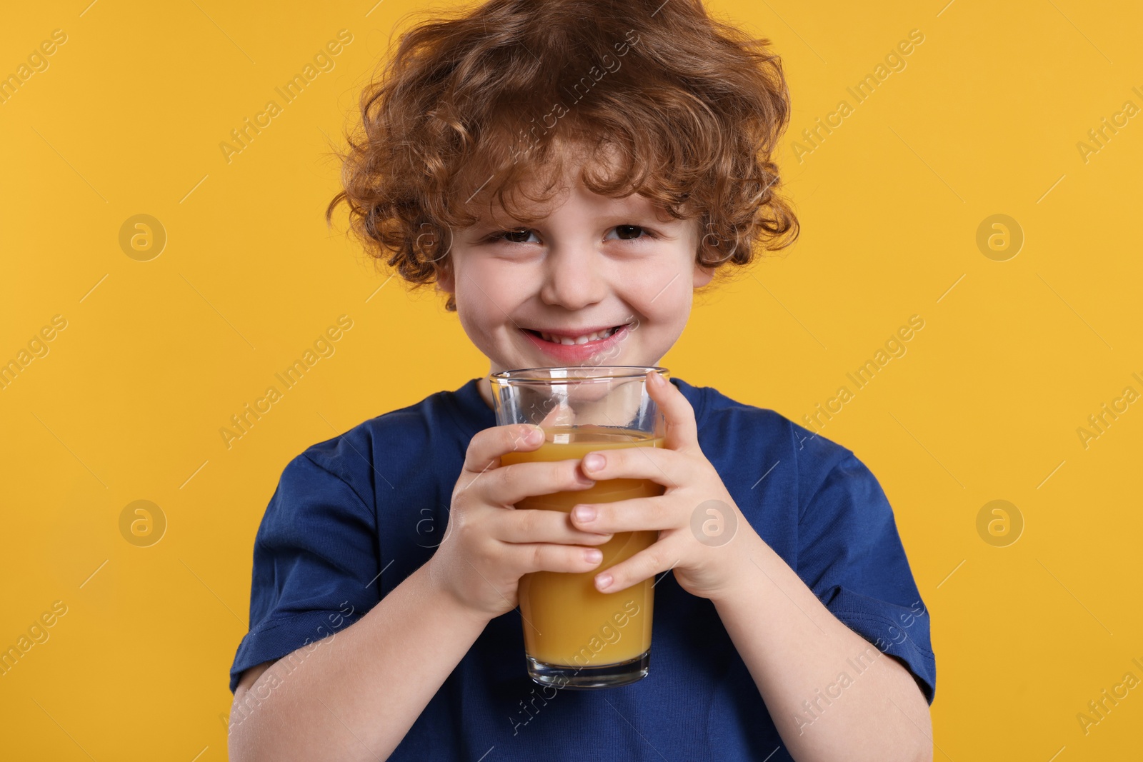 Photo of Cute little boy with glass of fresh juice on orange background