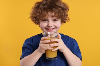 Cute little boy with glass of fresh juice on orange background