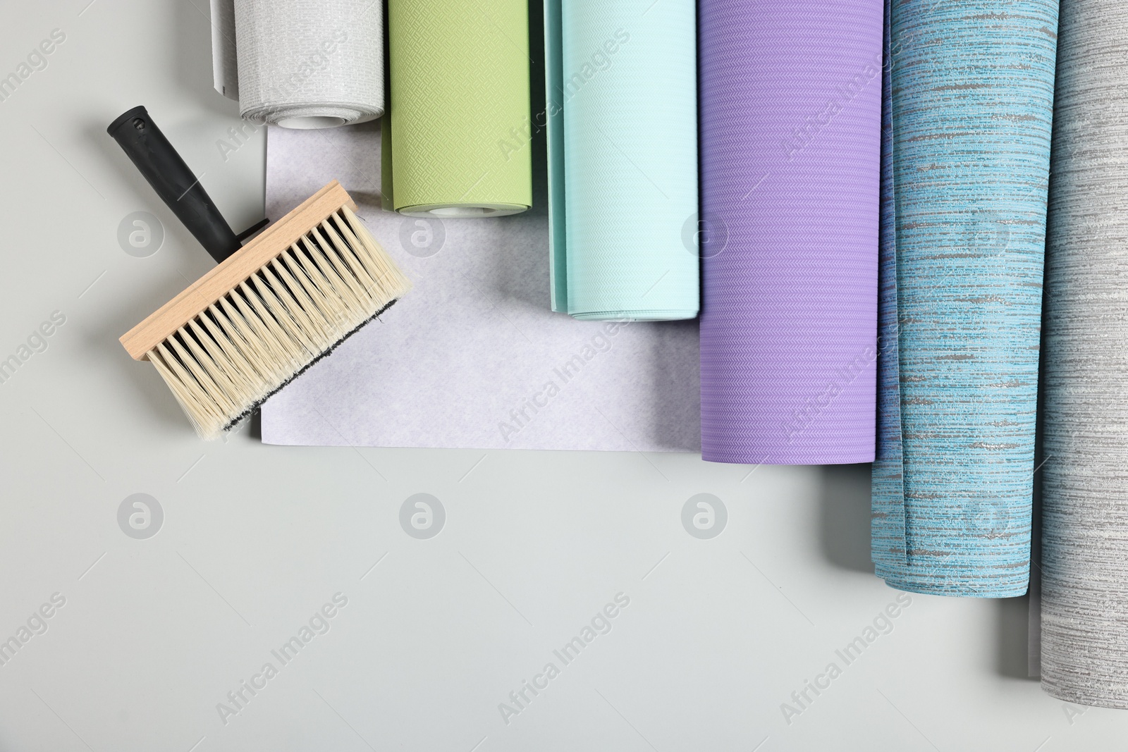 Photo of Different wallpaper rolls and brush on light background, flat lay. Space for text