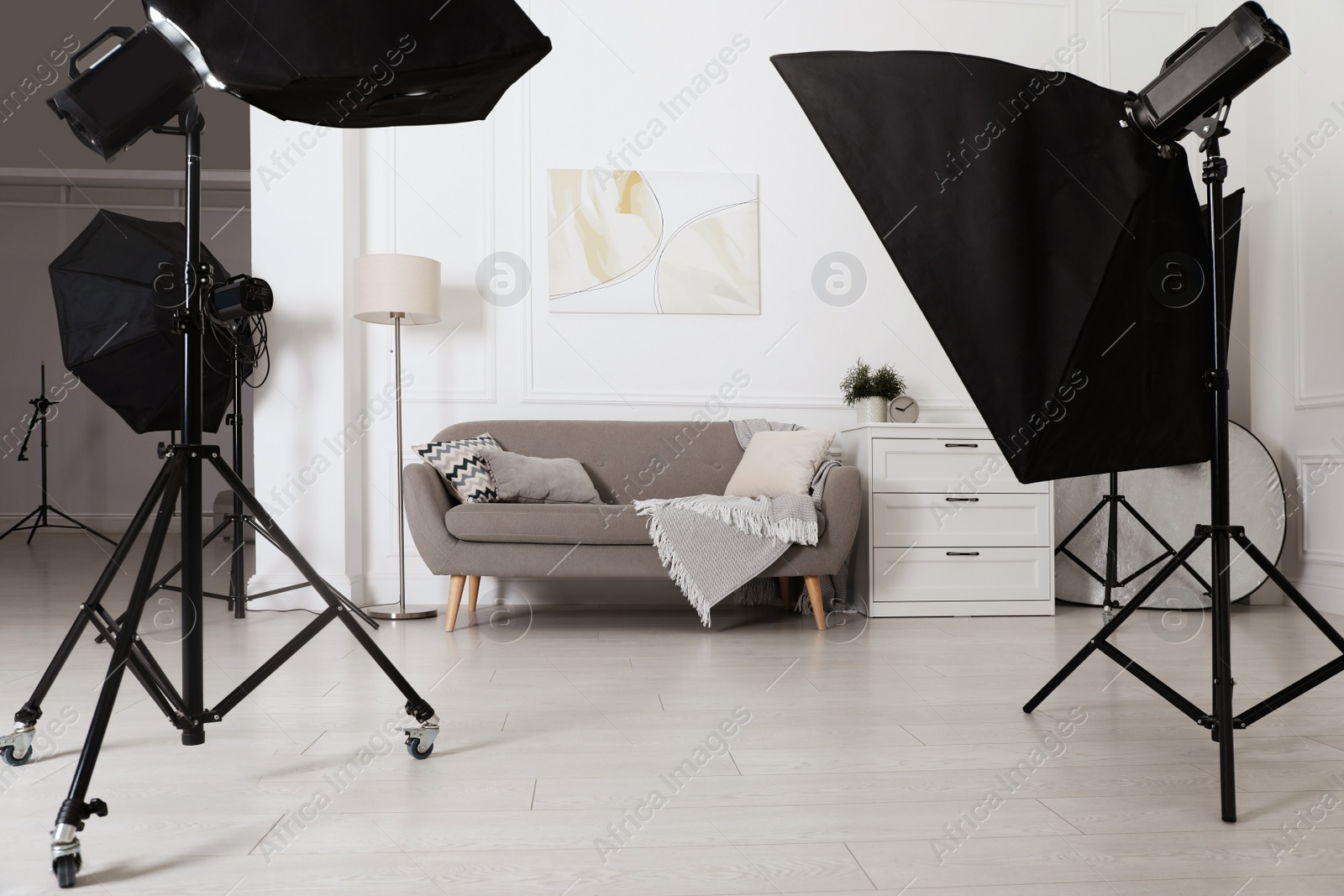 Photo of Set of stylish furniture surrounded by professional lighting equipment in photo studio. Cozy living room interior imitation