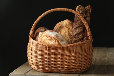 Photo of Wicker basket with different types of fresh bread on wooden table