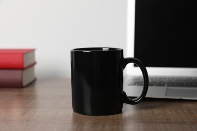 Photo of Black ceramic mug and laptop on wooden table at workspace