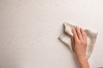 Photo of Woman wiping white wooden table with kitchen towel, top view. Space for text