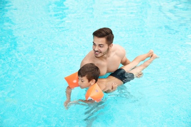 Father teaching son to swim with inflatable sleeves in pool