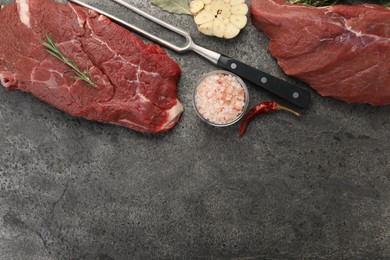 Photo of Piece of raw beef meat, spices, rosemary and fork on grey table, flat lay. Space for text