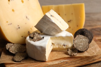 Photo of Board with delicious cheeses and fresh black truffles on wooden table, closeup