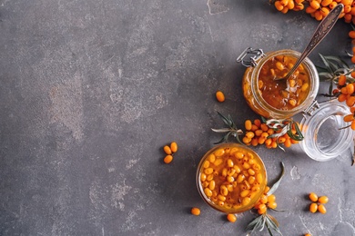 Delicious sea buckthorn jam and fresh berries on grey table, flat lay. Space for text