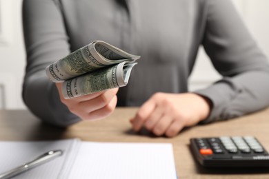 Photo of Money exchange. Woman holding dollar banknotes at wooden table, closeup