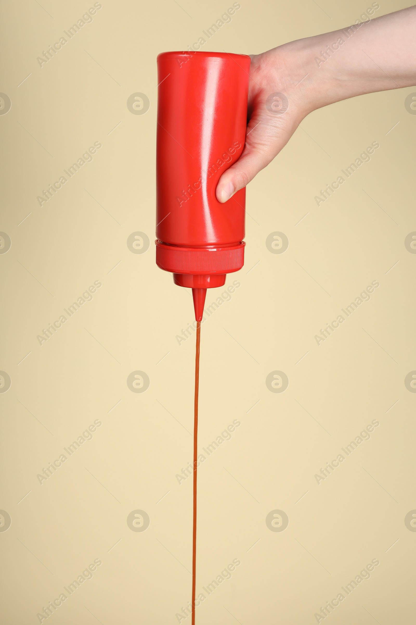 Photo of Woman pouring tasty ketchup from bottle on beige background, closeup