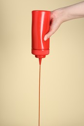 Woman pouring tasty ketchup from bottle on beige background, closeup