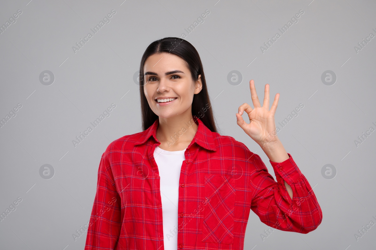 Photo of Young woman with clean teeth smiling and showing ok gesture on light grey background