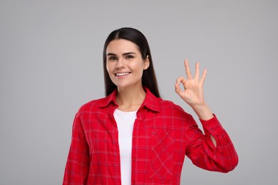 Young woman with clean teeth smiling and showing ok gesture on light grey background