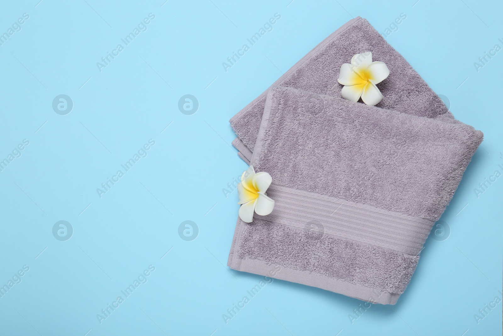 Photo of Violet terry towel and plumeria flowers on light blue background, top view. Space for text