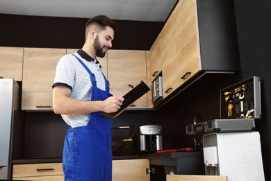 Photo of Male plumber with clipboard in kitchen. Repair service